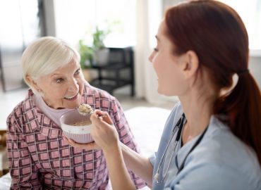 Caring nurse feeding aged woman in the morning