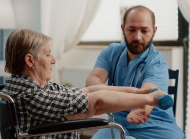 Nurse assisting disabled patient with physical exercises for recovery